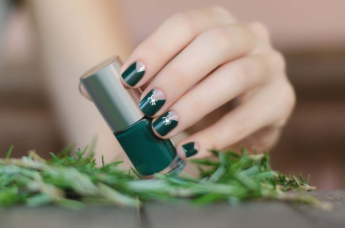 Female hand with green nail design holding nail polish bottle